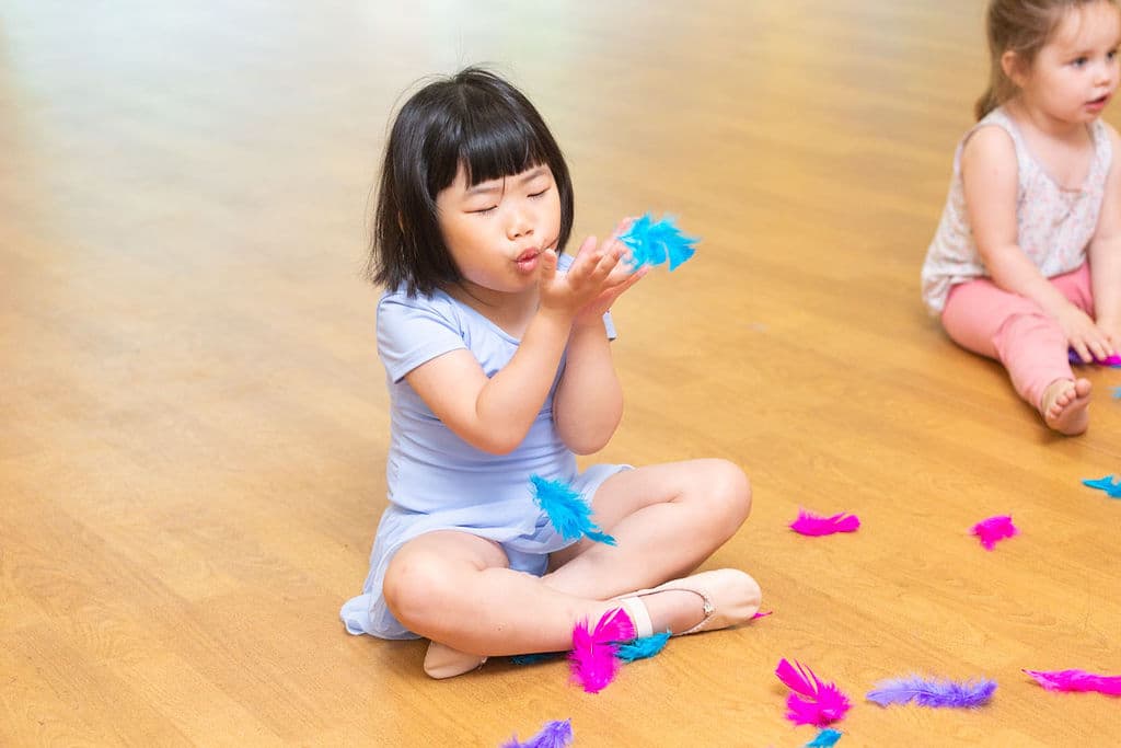 A Tiny Ballet dancer blowing a blue feather in class at En Pointe Cardiff